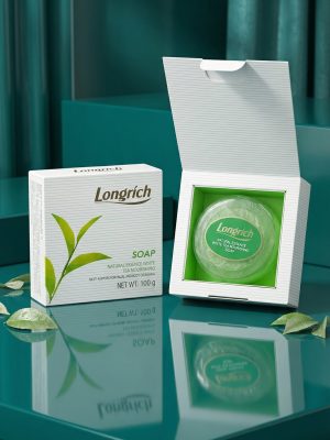 Longrich soap packaging on a reflective teal surface with green leaves.