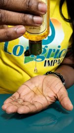 Hand holding a bottle of oil with a dropper, wearing a yellow shirt with text.
