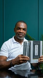 Man holding a silver tumbler and its packaging against a teal background